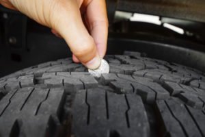 Person putting a coin in between tire tread to illustrate the depth.