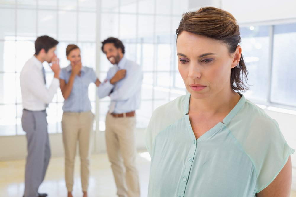 A woman looking sad while being made fun of at work.