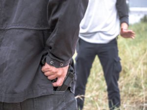 Dos personas discutiendo, y una está alcanzando un arma en un posible intento de asesinato