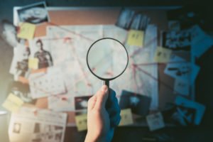 A person using a magnifying glass on a board filled with evidence.