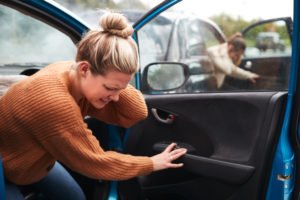 Two women climbing out of their vehicles after an auto accident, both holding their necks in pain.