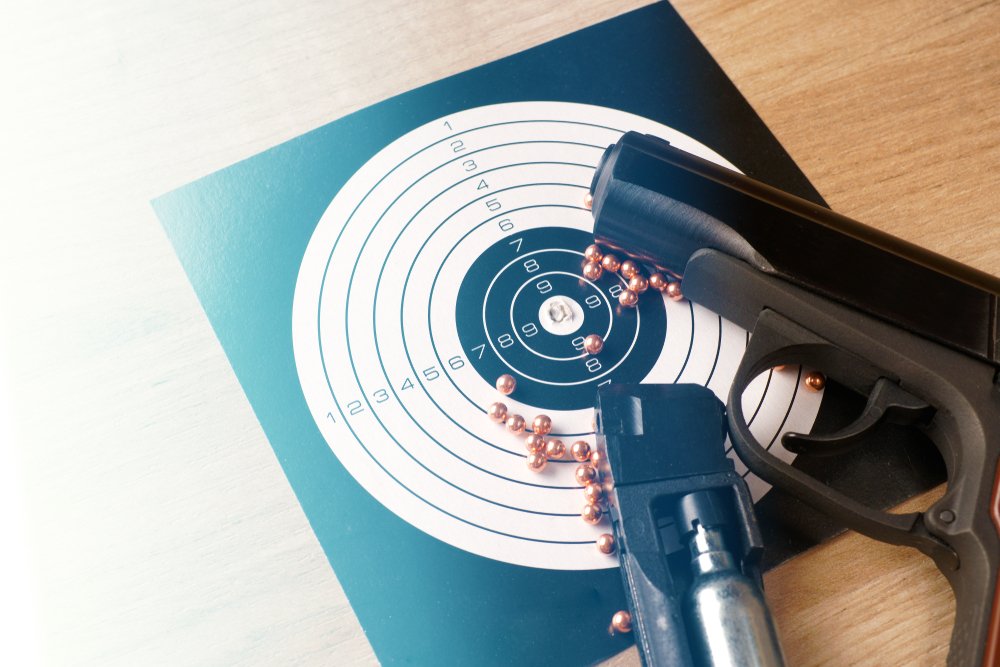 A BB Gun next to some BBs as well as a small paper target.