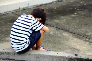 Child crouching alone on a curb unattended