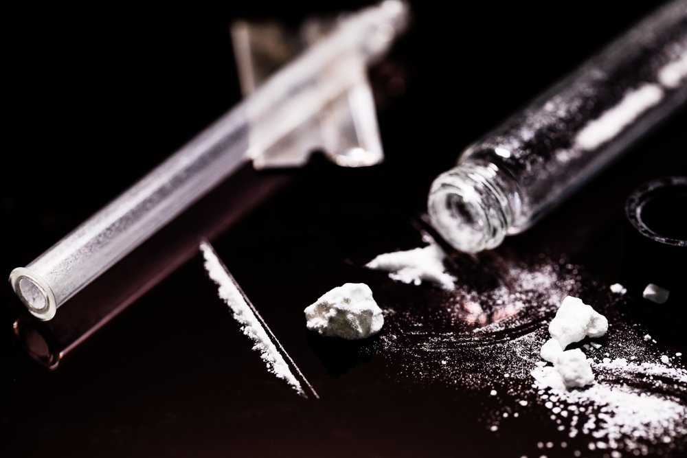A cocaine vial, and a glass straw used to snort cocaine, laid out on a mirror table top.