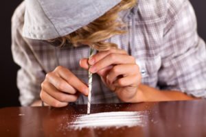 Hooded person hunching over table shorting cocaine