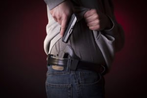 A man pulling his gun out of its holster, that was concealed by his jacket