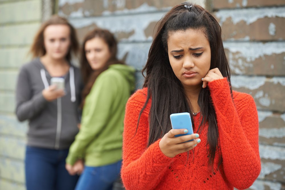 A teenage girl looking sad on her smartphone.