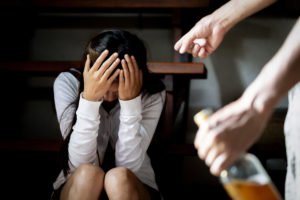 DV victim on couch as abuser drinks beer