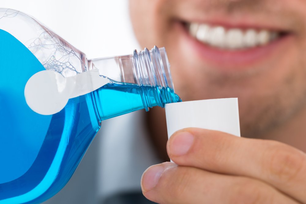 Man smiling as he pours himself a cap full of Listerine mouthwash.