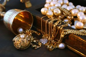 A jewelry box overfilled with gold and pearl jewelry.