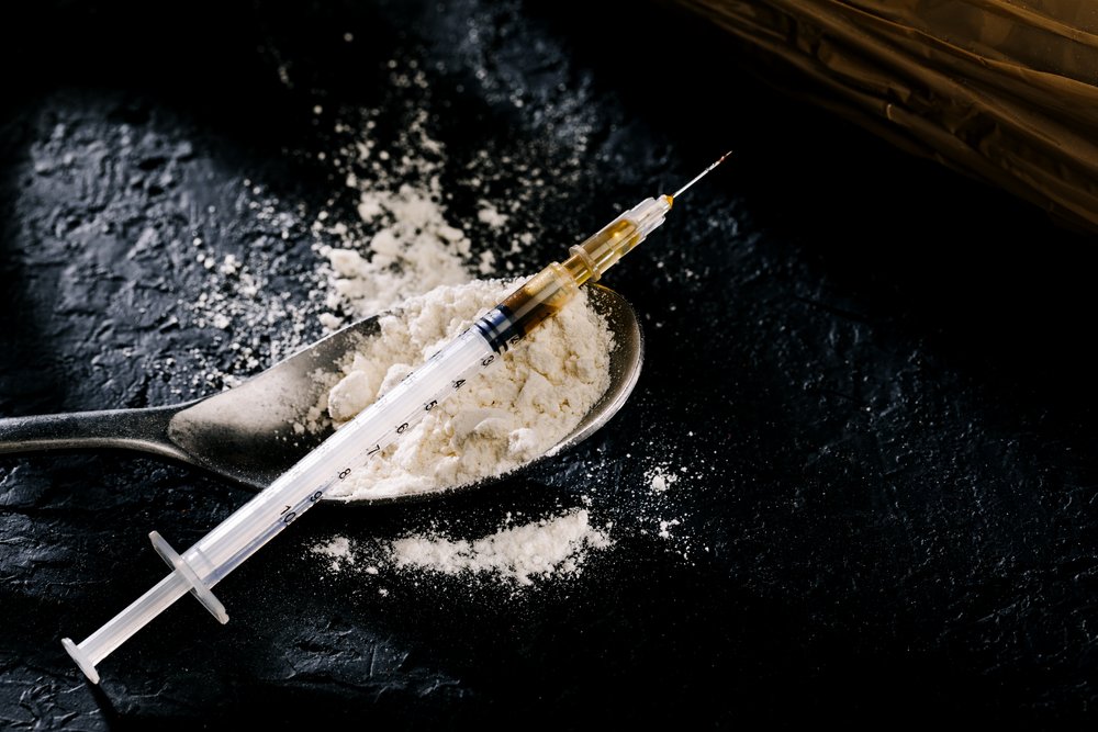 A syringe of heroin on top of a spoon filled with heroin.