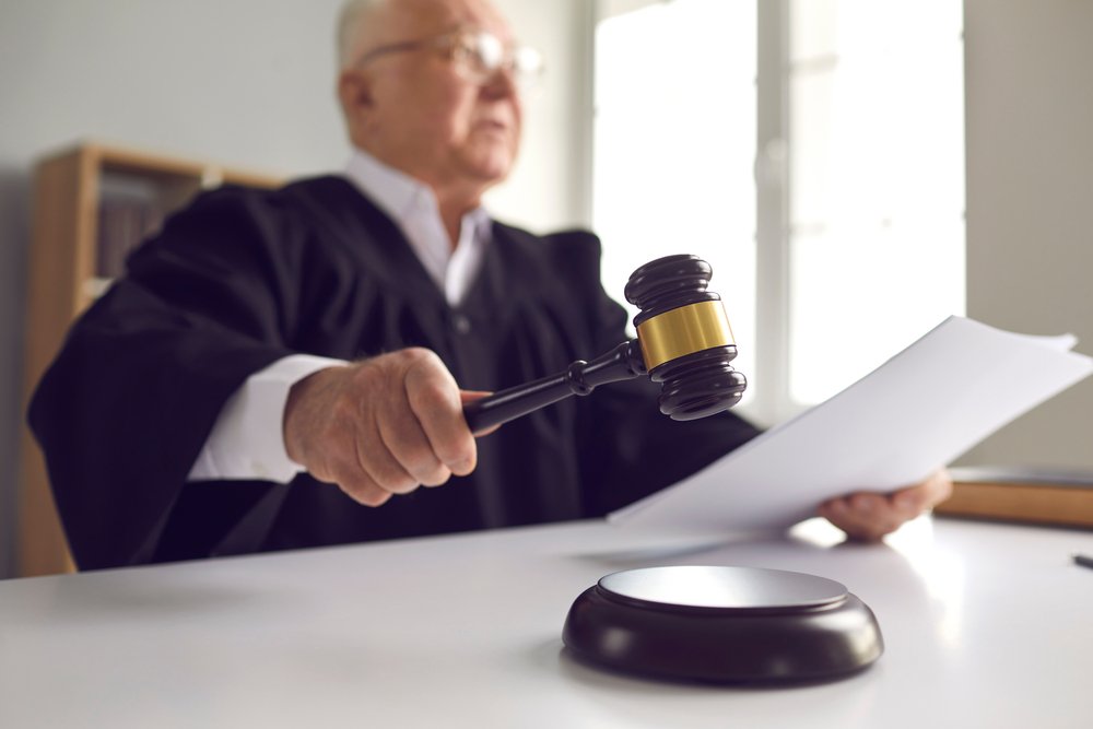 A judge holding documents with a gavel in his hand.