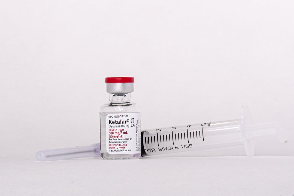 A vial of ketamine next to a syringe.