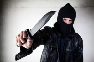 A masked man pointing a knife.