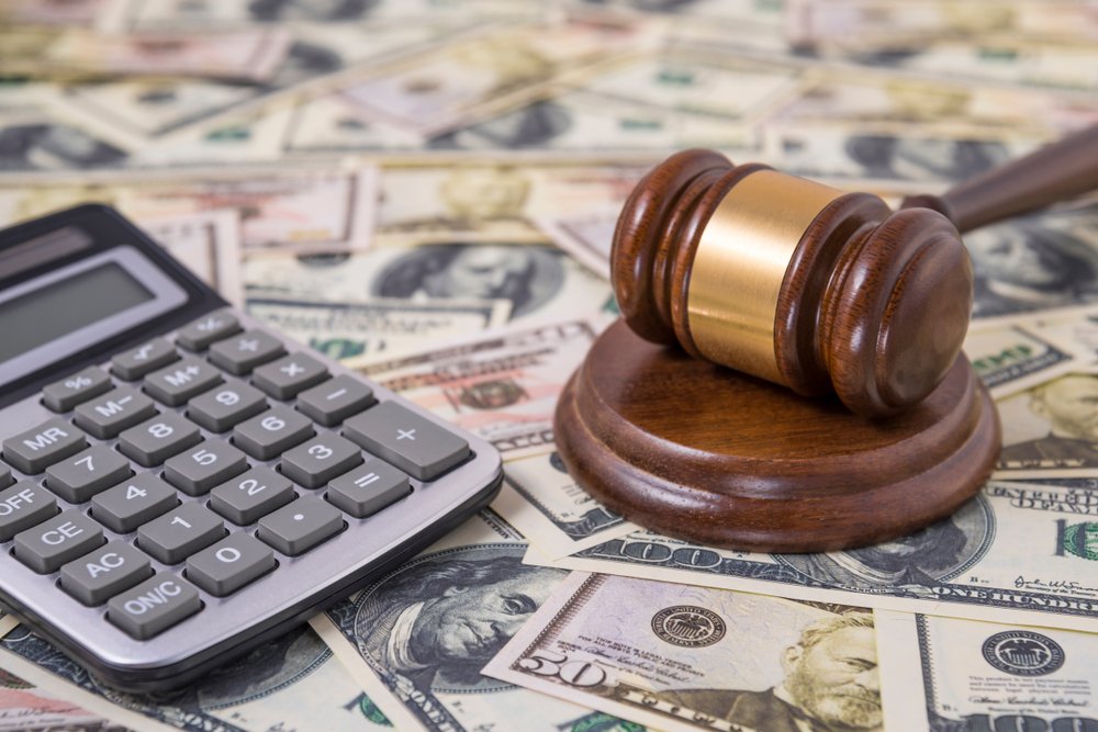 A gavel and a calculator laying on a table of money.