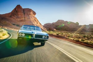 A man driving a sleek old-school convertible through the Nevada desert, possibly drunk driving.