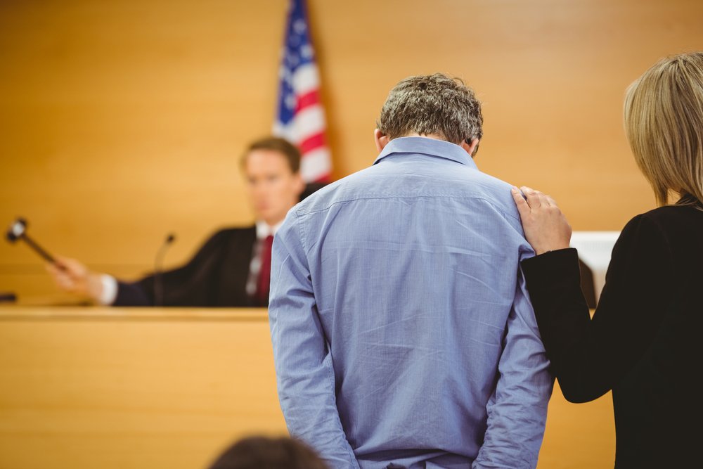 A man looking down while his defense attorney speaks with the judge.