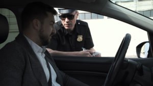 A man being questioned by a police officer in his car.