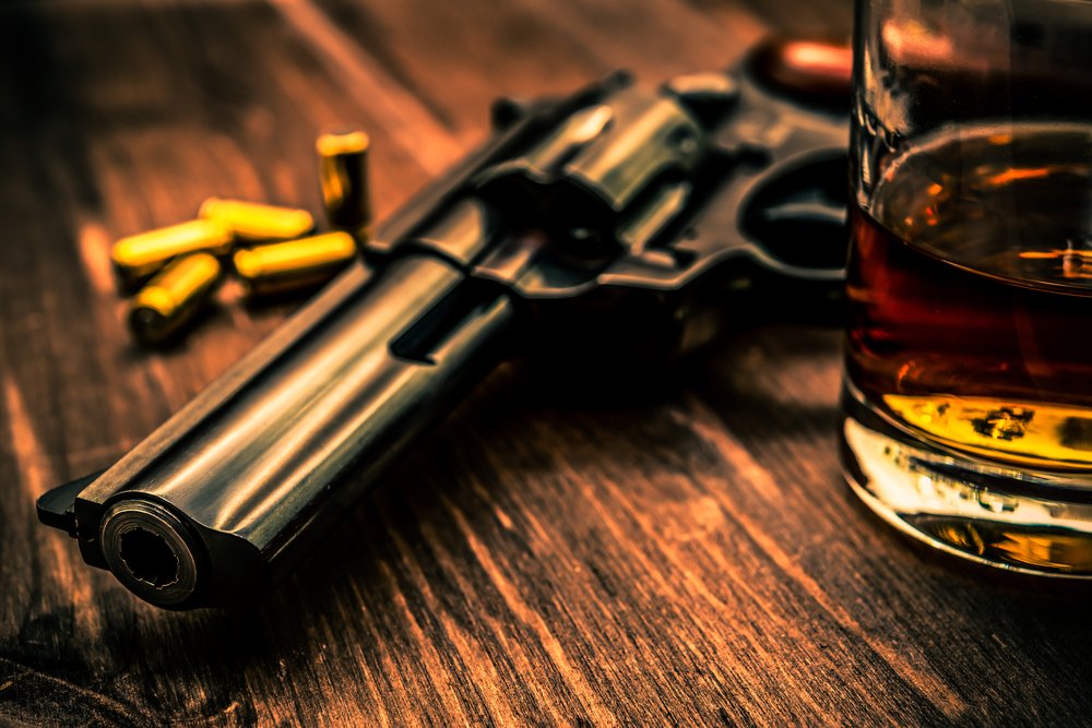 A gun sitting on a table next to a glass of whiskey.