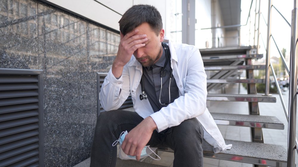 A physician in despair, sitting on stairs.