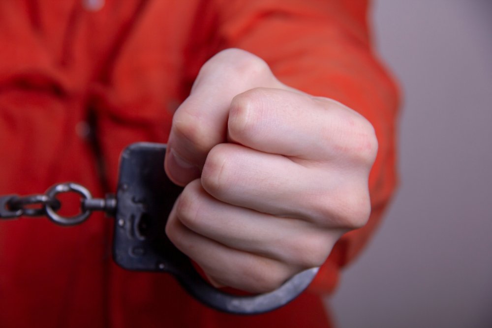 A teenager in handcuffs, wearing orange prison garb.