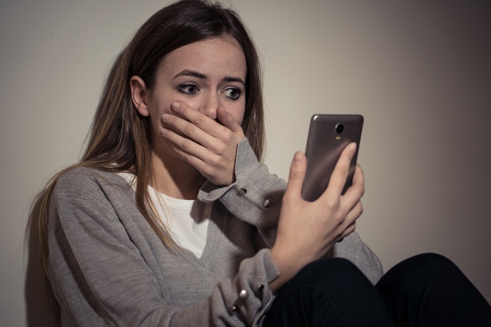 A young woman shocked by what she sees on her phone, representing online harassment.