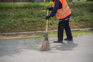 A man in an orange vest sweeping a public walkway.