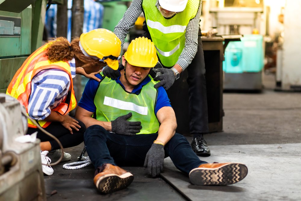 Un trabajador de la construcción con un casco de seguridad yace en el suelo después de haber sido gravemente herido mientras dos colegas lo atienden