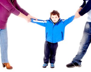 A young child being pulled in different directions by parents.