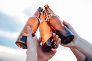 Three people holding up beer bottles to sky