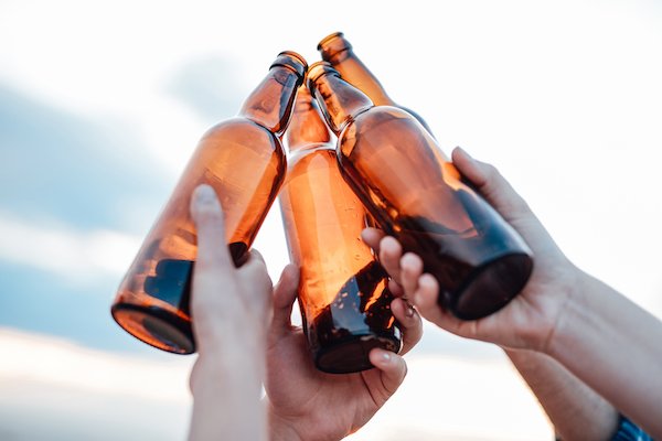 Three people holding up beer bottles to sky