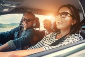 Smiling parents driving a car with their child in the backseat.