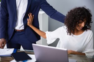 Woman at desk pushing away boss harassing her