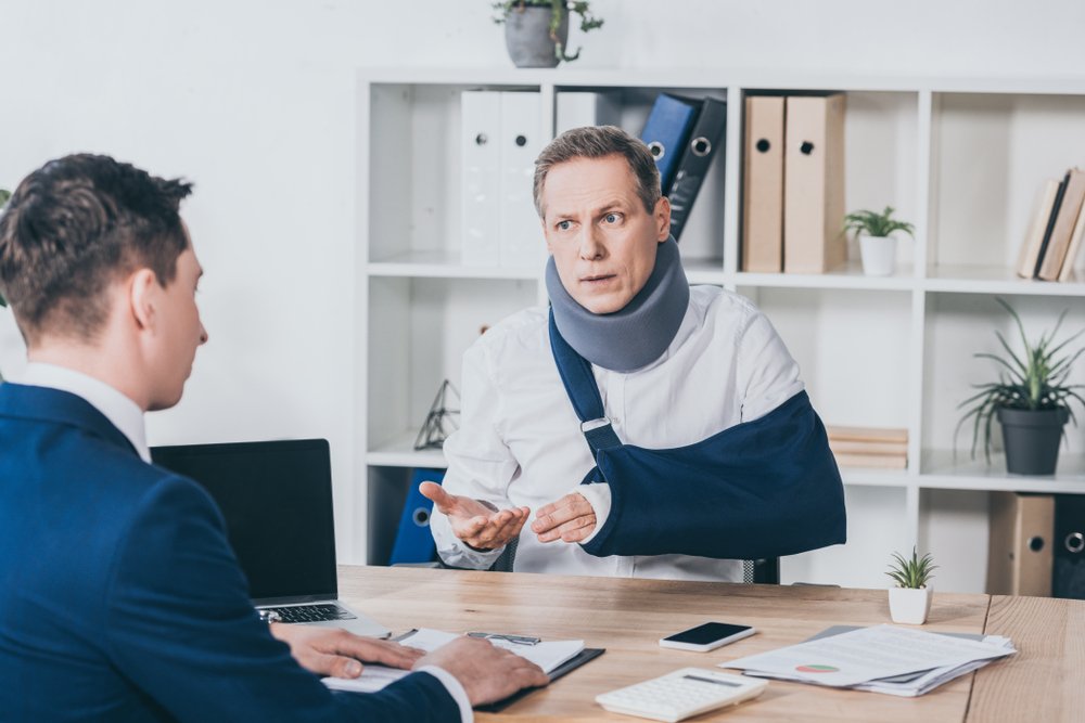 A man wearing a neck brace as well as a cast on his arm, speaking with his attorney regarding his claim.