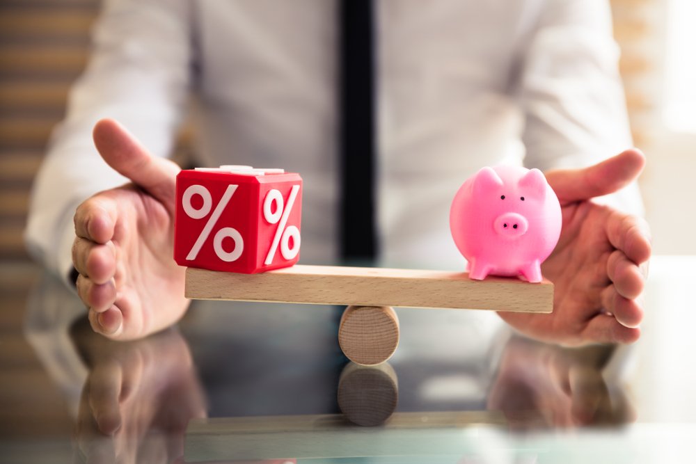 A seesaw with a piggy bank on one side and a percentage cube on the other.