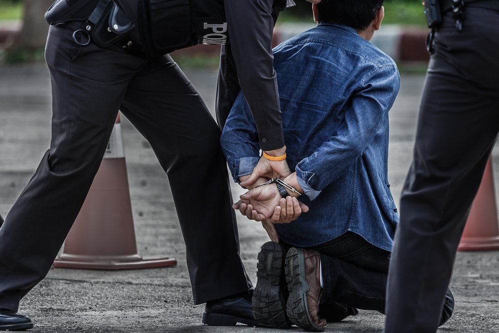 Policía colocando a un hombre arrestado de rodillas.