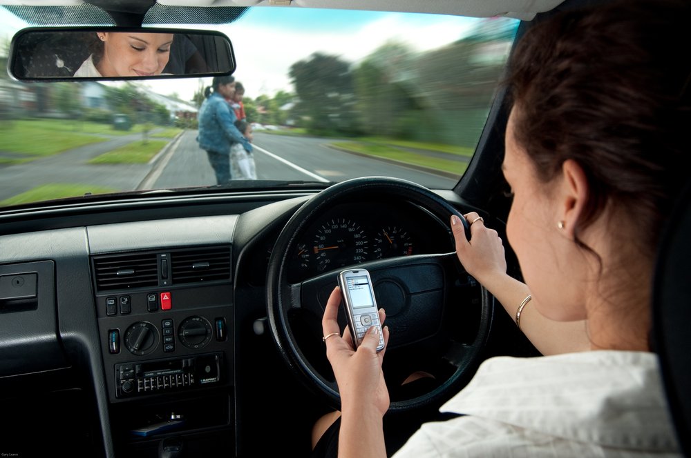 A woman texting and driving while pedestrians are crossing the street in front of her.