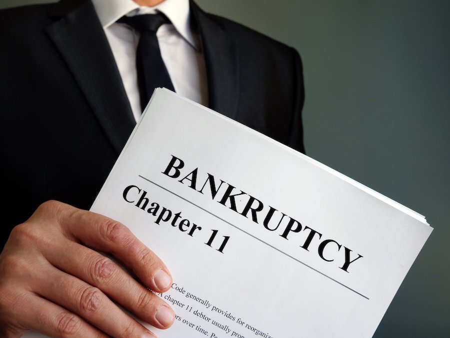 Man in business suit holding paper that says "bankruptcy chapter 11"