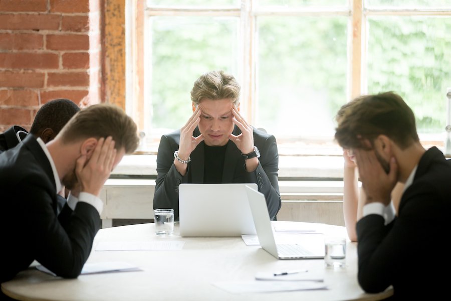 Board meeting of worried board members looking at laptops