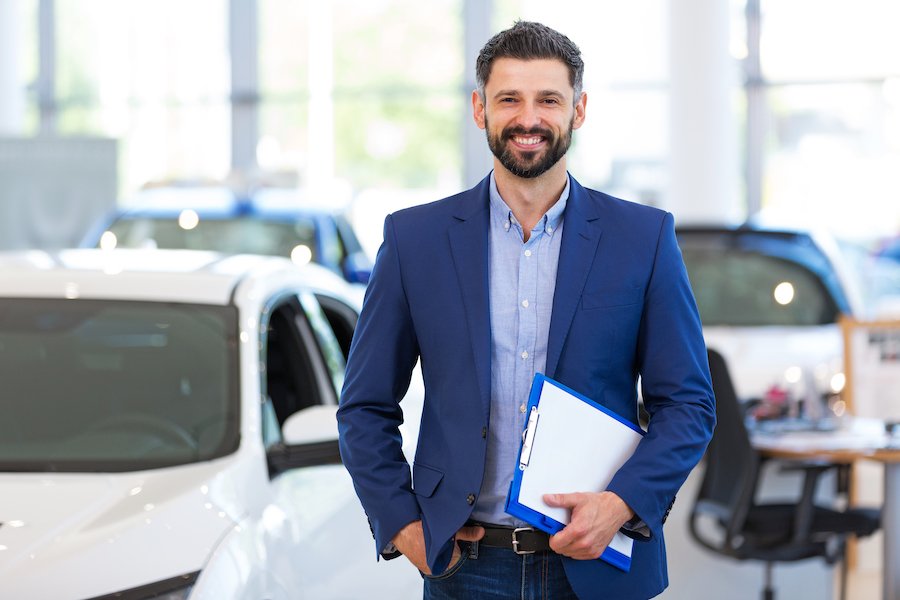 Vendedor de automóviles sonriente junto al inventario