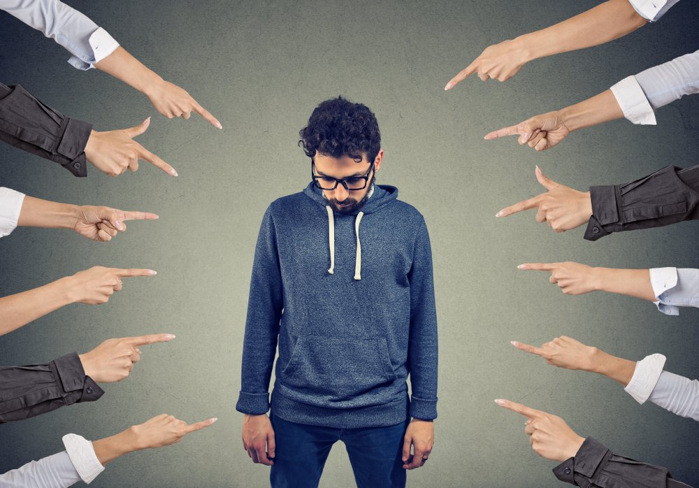 Multiple hands pointing at a man looking down in embarrassment.