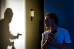 A man holding his gun as a burglar walks through his home with a gun.
