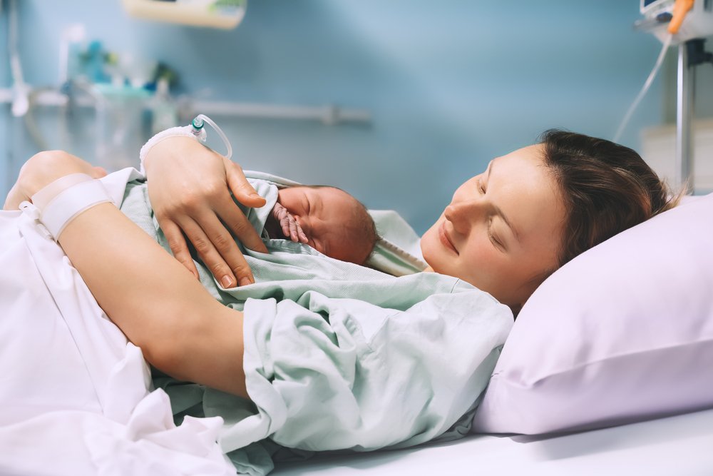 Una madre con su recién nacido en una cama de hospital, posiblemente en una licencia de ausencia del trabajo.