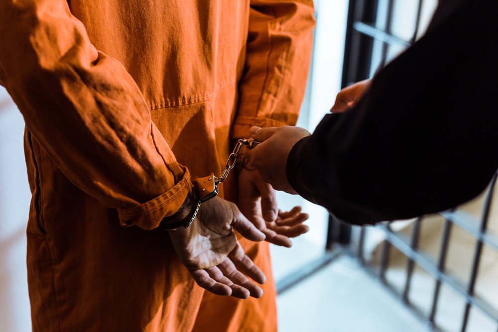 A prisoner in handcuffs being led by a prison guard.