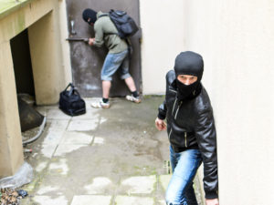 A masked man serving as a lookout for another masked man who is trying to break into a building, as a possible example of accessory before the fact.