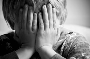 Close-up of a young child covering his face with his hands as a sign of anguish, possibly due to abuse.