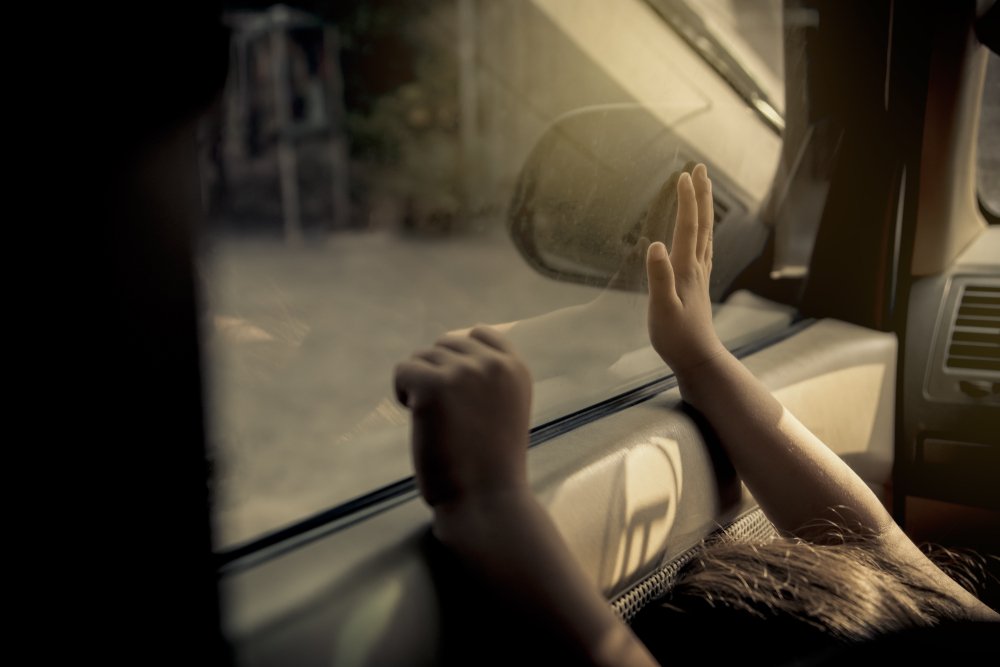 A child holding up her hands against a closed window of a hot car. One possible example of a death that could be the result of a negligent homicide.