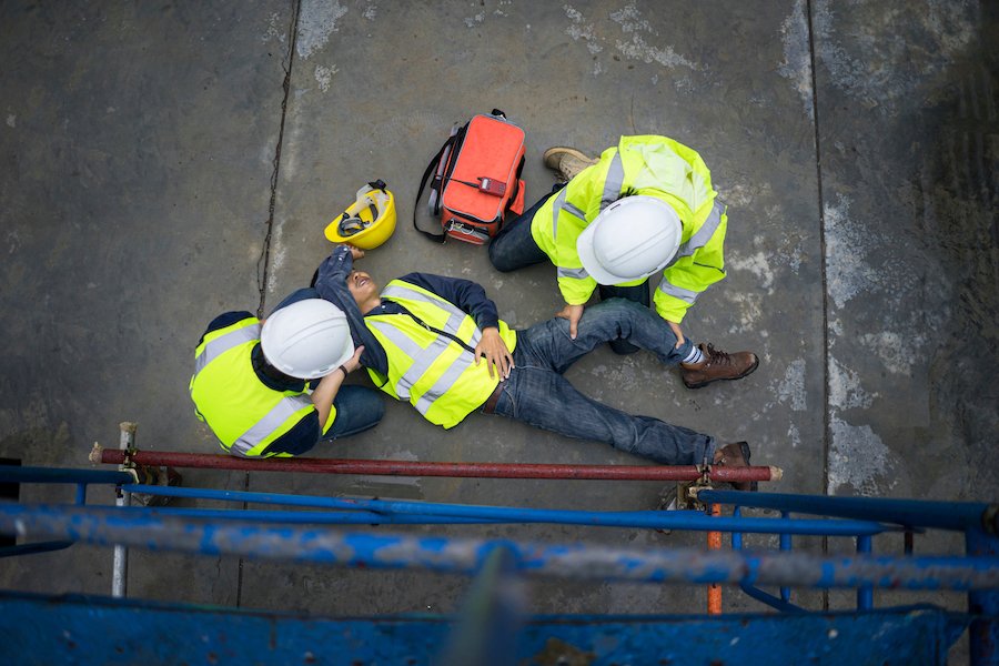 Secuelas de un accidente de construcción con trabajadores con cascos de protección ayudando a la víctima en el suelo