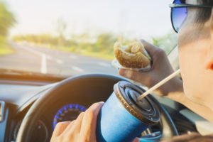 A young man eating and drinking a soda while driving a car.