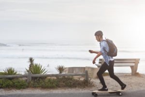 A young man riding on an electric skateboard by the beach.